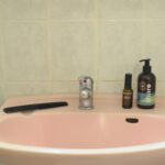 A pink ceramic washbasin with hygiene products and a comb on a tiled wall.